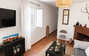 A living room with a TV, a fireplace, a sofa, a coffee table, and a window with curtains. - La Casilla - El Mirador de Gérgal - Rural Living (Gérgal)
