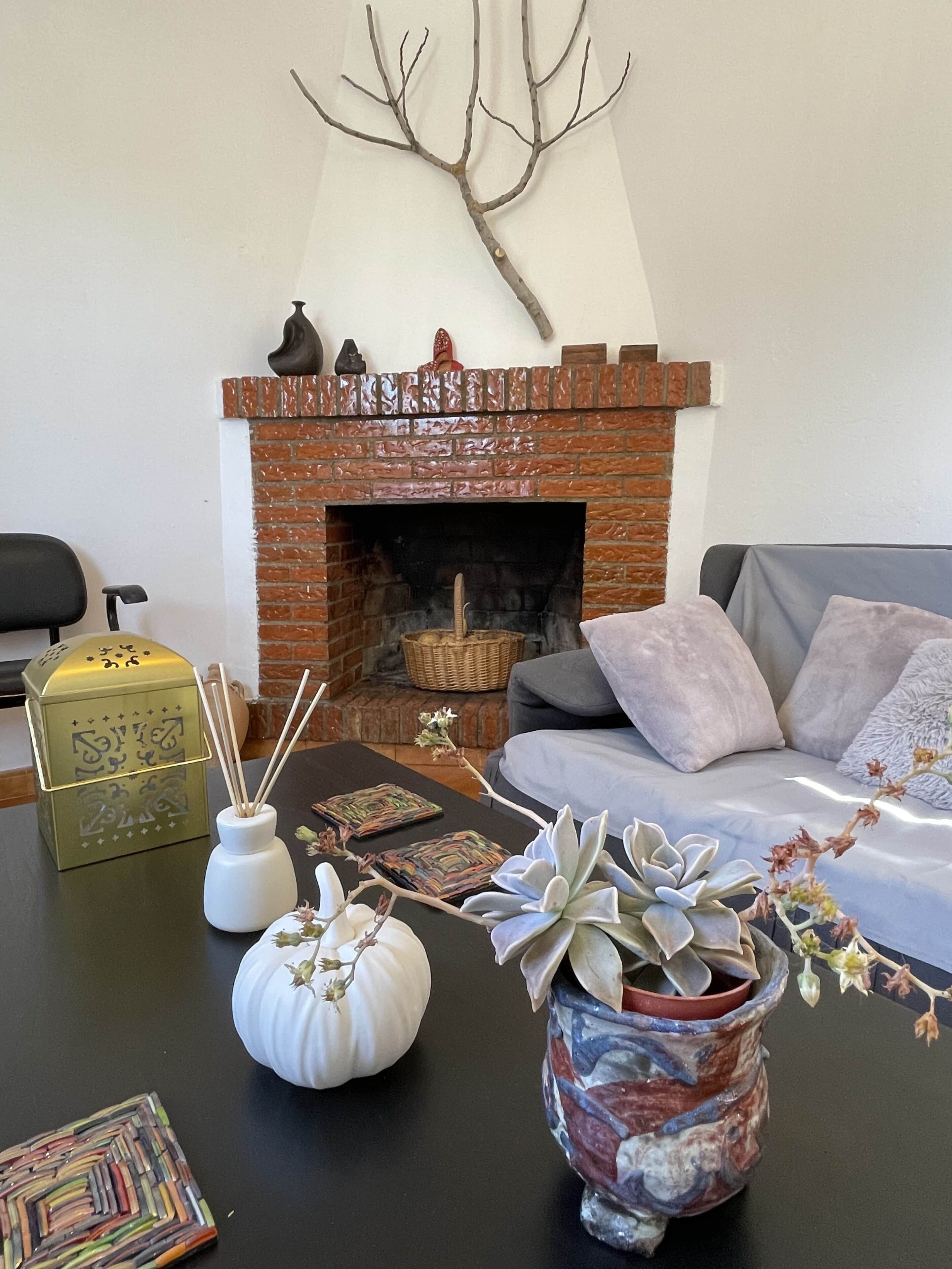 Uma sala de estar com lareira de tijolos, um sofá, vasos decorativos e uma mesa com diversos objetos.