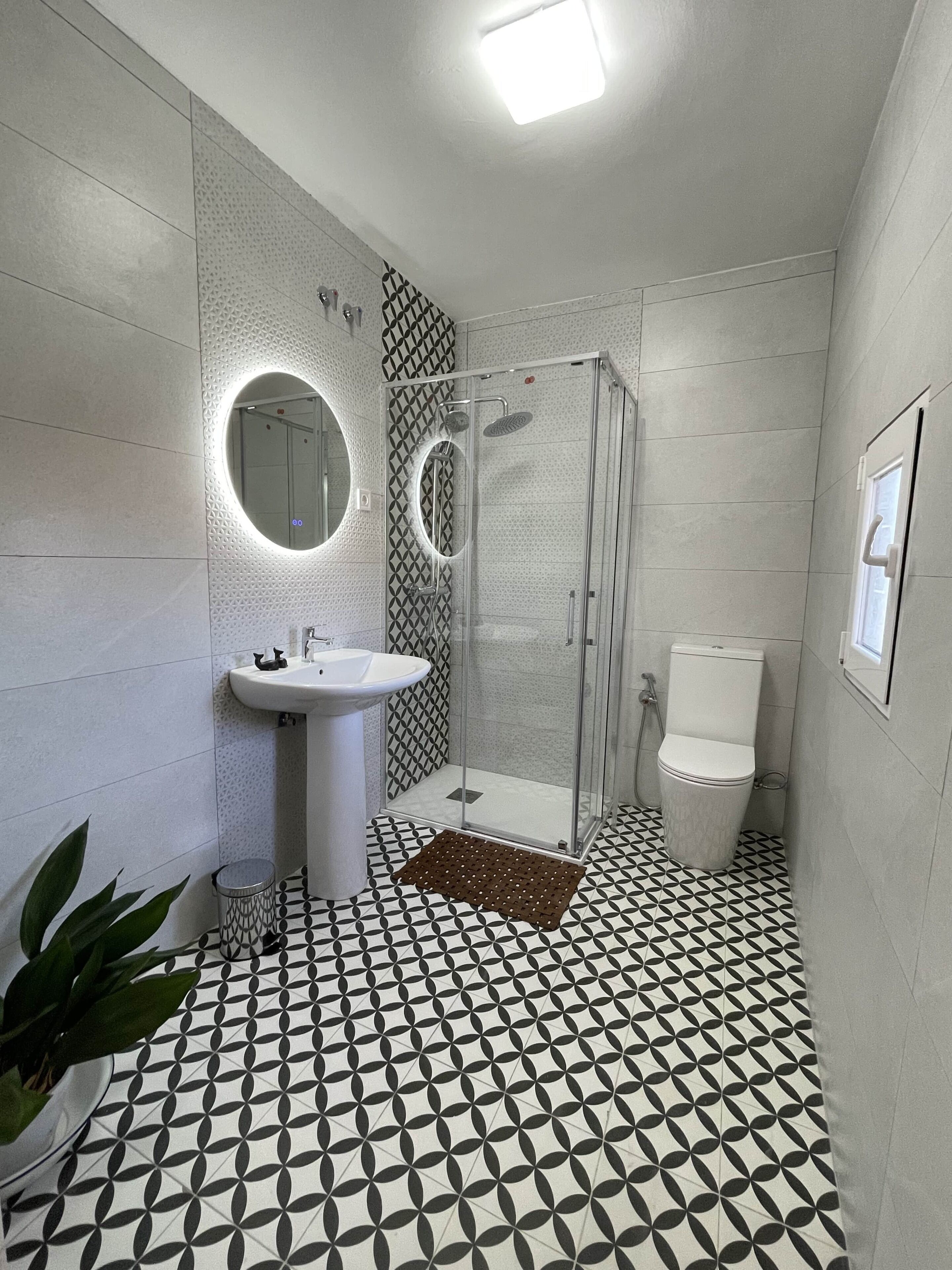 Une salle de bain avec un lavabo blanc, des toilettes, un espace douche et un carrelage décoratif.