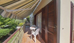 Een balkon met een tafel en stoelen, een houten deur en uitzicht op groen.