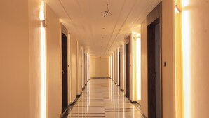 A long, well-lit hallway with doors on both sides, leading to individual rooms. - Srushti Resort (Gangapur)