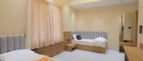 A modern hotel room with two beds, a small wooden bench, a bedside table, and a mirror.