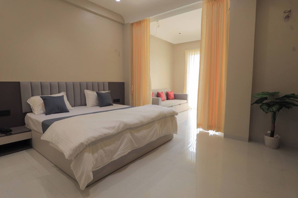 Quarto de hotel moderno com cama grande, mesas de cabeceira, um sofá e um vaso de plantas.