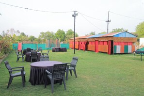 An outdoor area with tables and chairs, a covered seating area, and a building with colorful curtains.