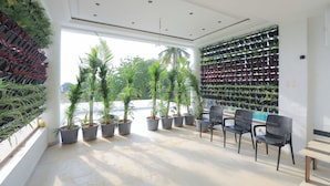 A room with potted plants, a seating area with chairs, and a wall with hanging planters. - Srushti Resort (Gangapur)