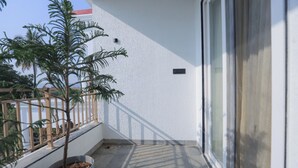 A balcony with a potted plant, a white wall, and a window. - Srushti Resort (Gangapur)
