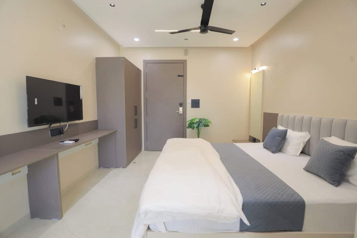 Quarto de hotel moderno com cama, escrivaninha, televisão, ventoinha de teto e porta.