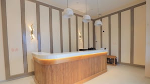 A reception desk with a wooden finish, pendant lighting, and a wall with vertical panels. - Srushti Resort (Gangapur)