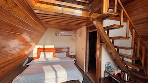 A wooden cabin room with a bed, a wooden staircase, and a small table with items on it. - The Woodshed (Mukteshwar)