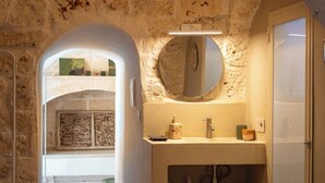 Ein Badezimmer mit Steinwand, rundem Spiegel, Waschbecken und Tür.