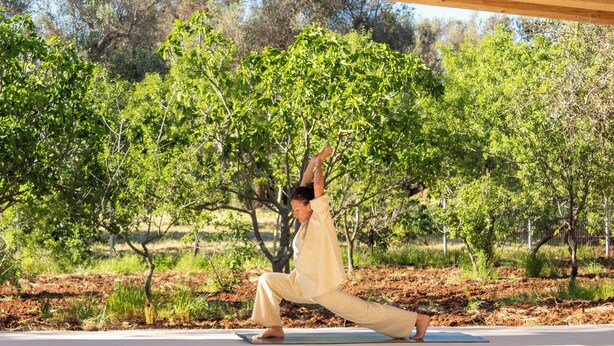 Eine Person übt Yoga unter einer Holzbeschaffenheit mit Bäumen im Hintergrund.