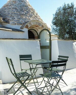 Eine Terrasse mit Tisch und Stühlen, eine Steinkuppel und ein Baum im Hintergrund.