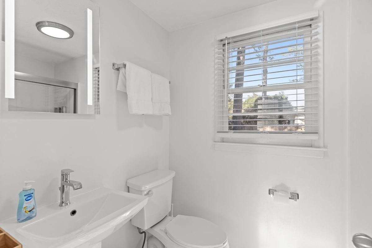 A bathroom with a white sink, toilet, and window with blinds.