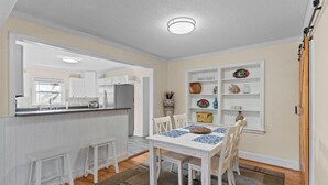 Una cocina con armarios blancos, una mesa de comedor con individuales azules y una pequeña isla con taburetes.