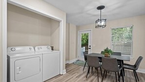 Un cuarto de lavado con lavadora y secadora, un comedor con mesa y sillas, y una ventana con persianas.