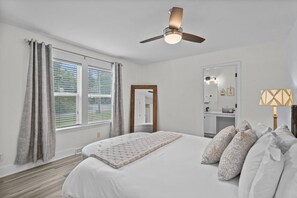 A bedroom with a bed, a ceiling fan, a window with curtains, a mirror, and a bedside lamp.