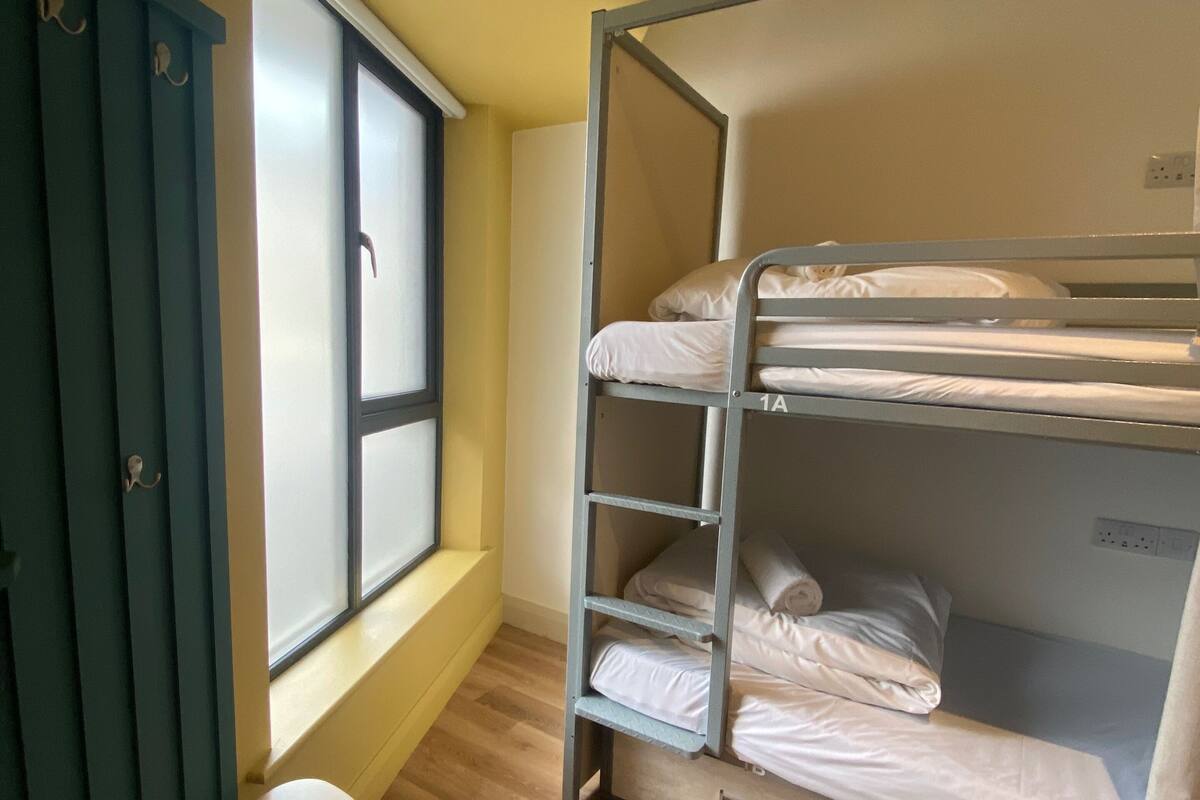 A bunk bed room with a window, a small table, and a door.