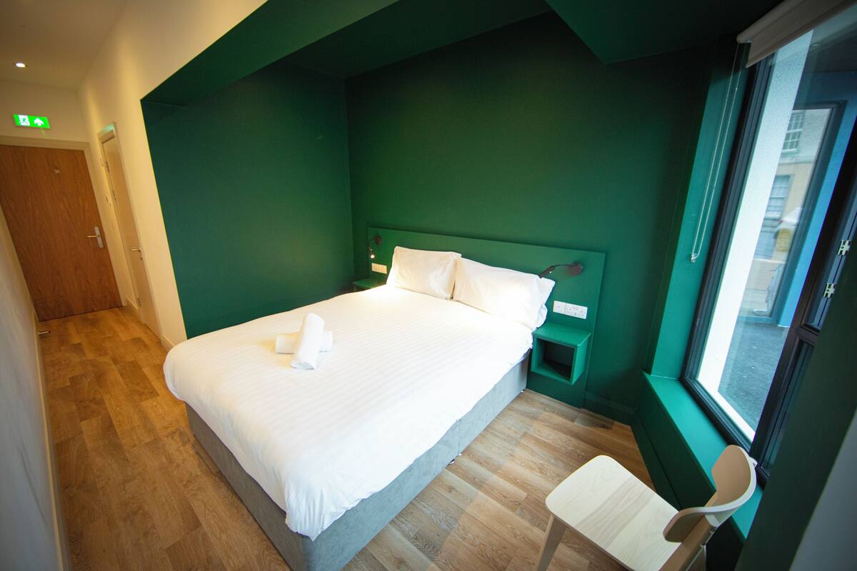 A hotel room with a bed, a nightstand, a chair, and a window.