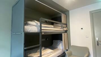 A bunk bed with two levels, a small chair, a trash bin, and a door.
