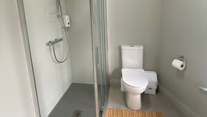 Un baño moderno con ducha de vidrio, inodoro y un tapete de madera en el suelo.