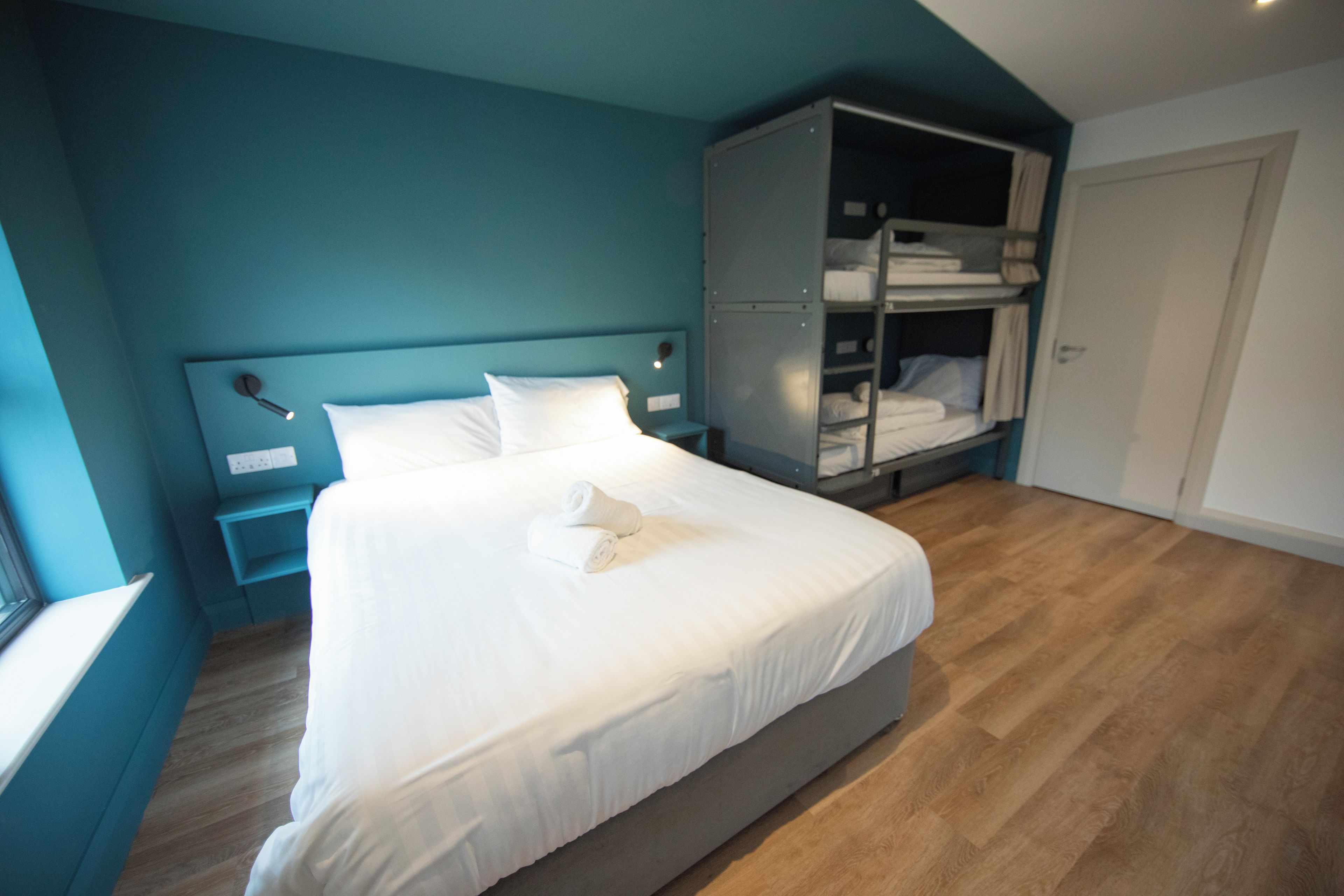 A neatly made bed in a room with teal walls and wooden flooring.