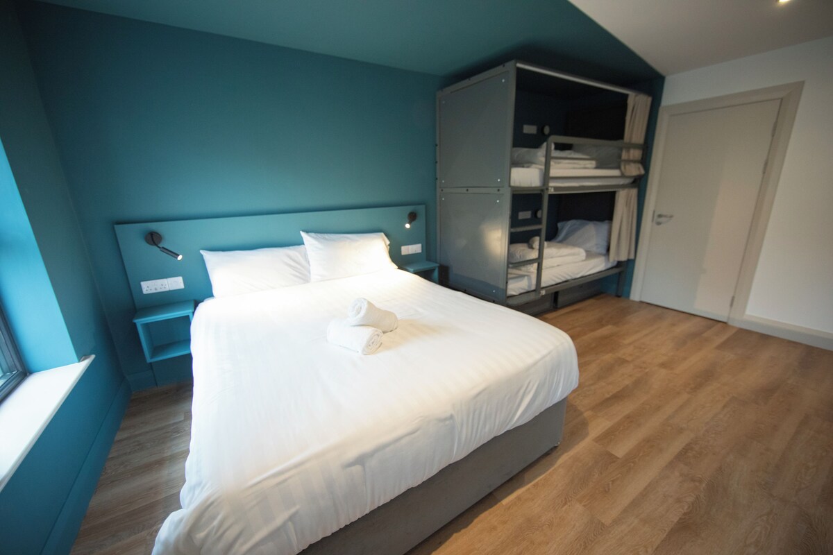 A neatly made bed in a room with teal walls and wooden flooring.