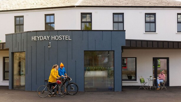 Un hostal llamado 'Heyday Hostel' con una fachada moderna, ventanas grandes y una zona de estar al aire libre.