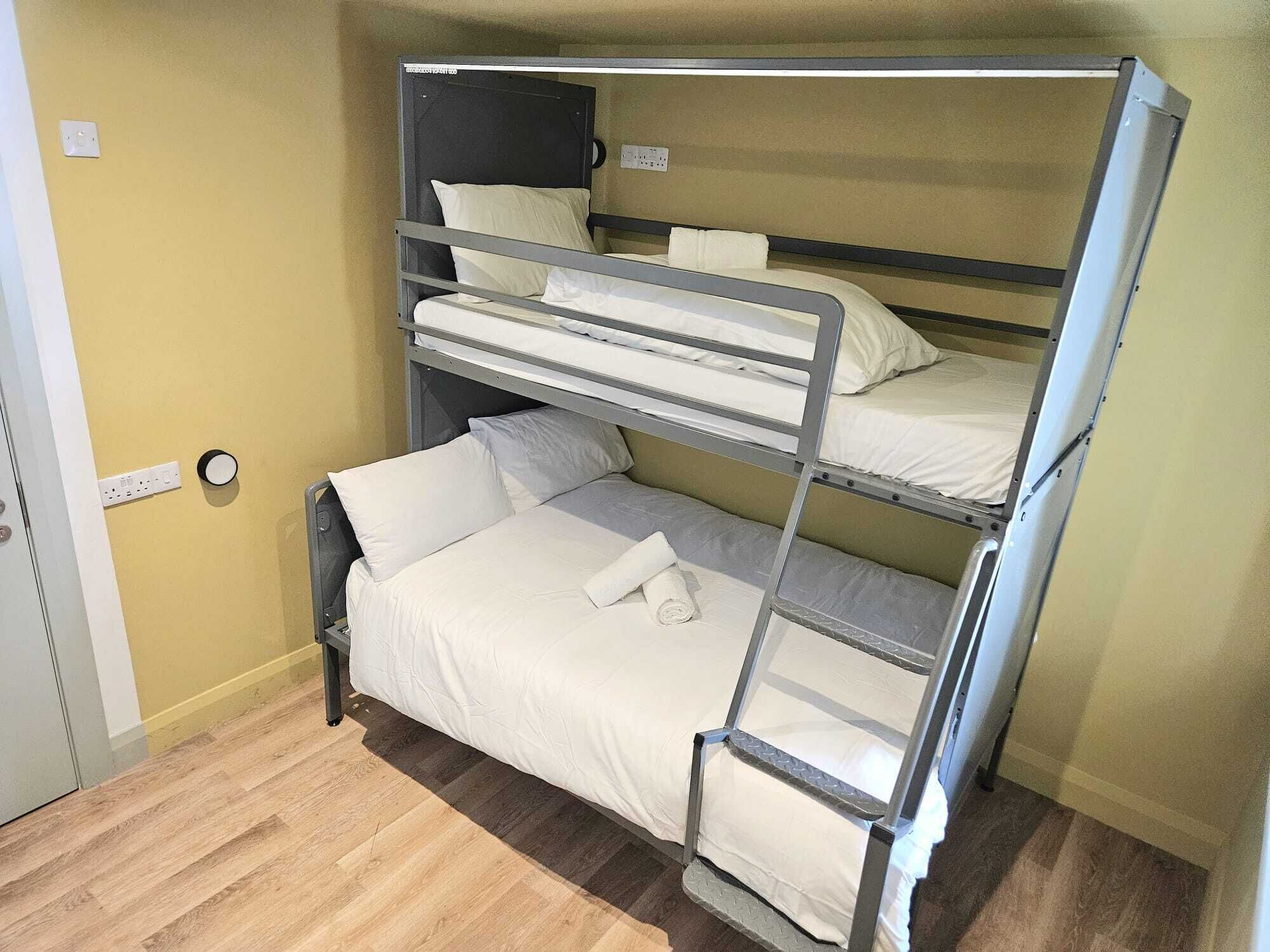 A bunk bed room with a wooden floor, a door, and a wall socket.
