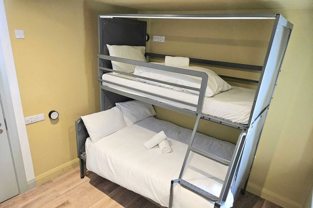 A bunk bed room with a wooden floor, a door, and a wall socket.