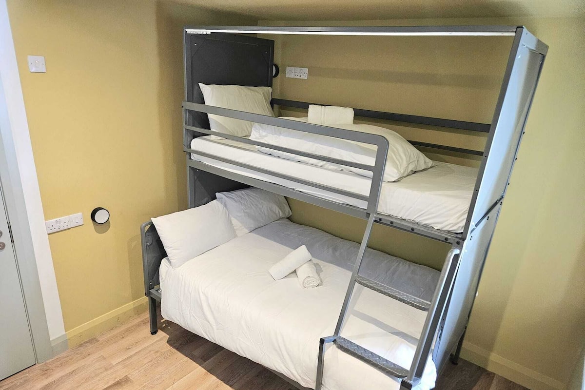 A bunk bed room with a wooden floor, a door, and a wall socket.