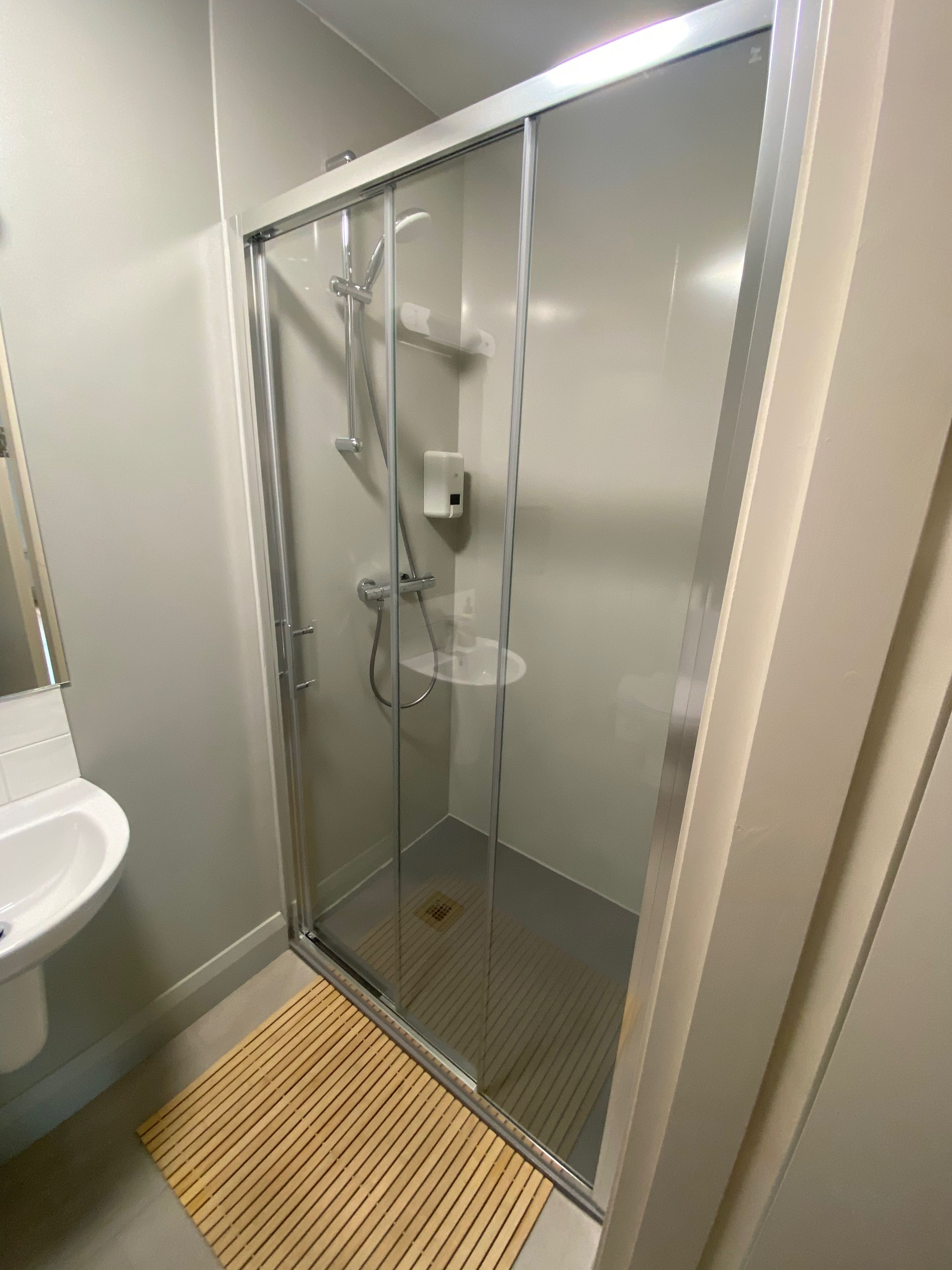 Une salle de bain moderne avec une douche à parois de verre, un lavabo blanc et un tapis en bois.