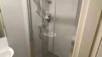 A modern bathroom with a glass-enclosed shower, a white sink, and a wooden mat.