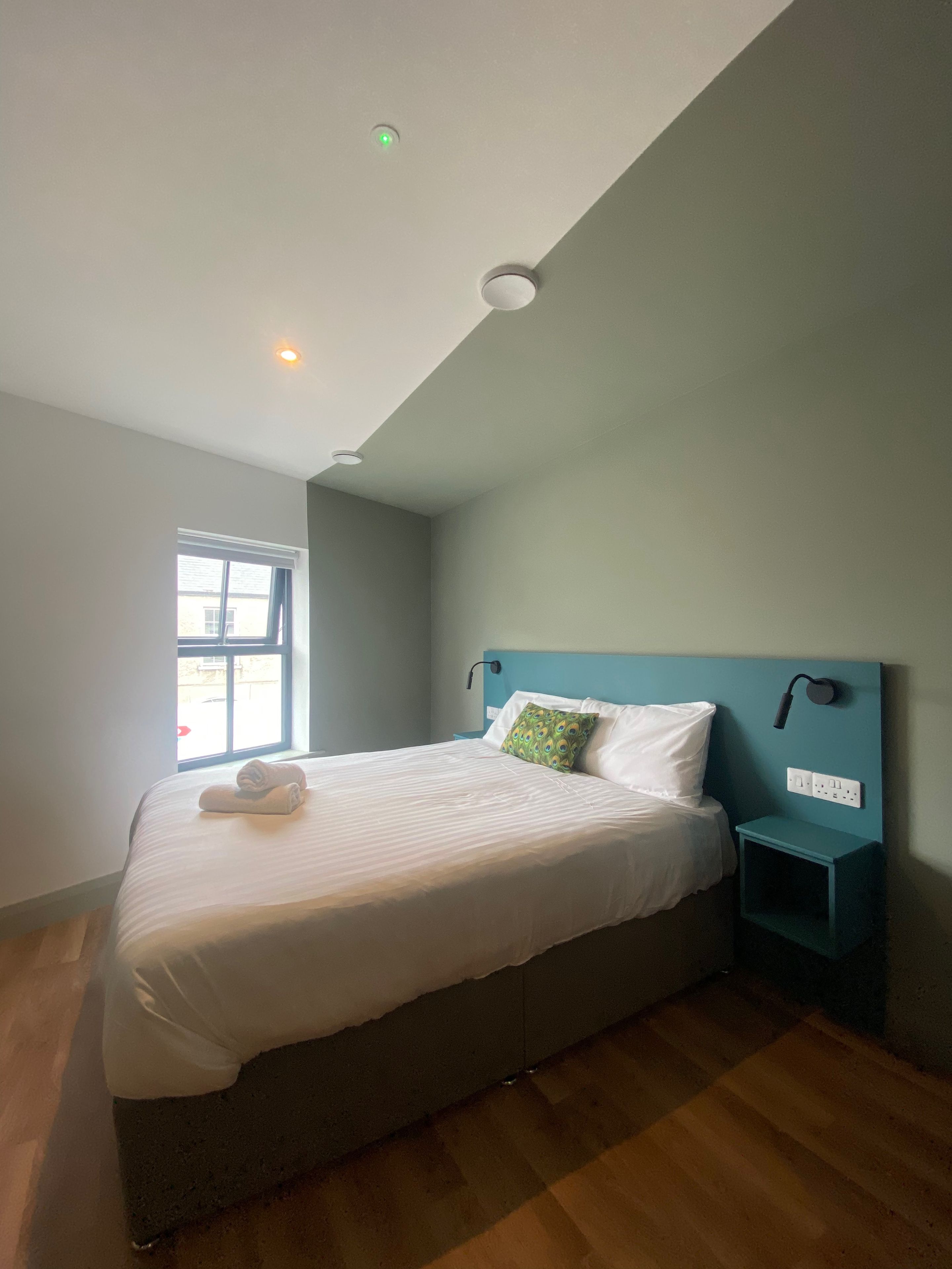 Una camera da letto con un letto, un comodino, una finestra e una lampada a soffitto.
