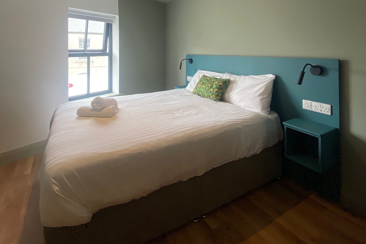 A bedroom with a bed, a nightstand, a window, and a ceiling light.