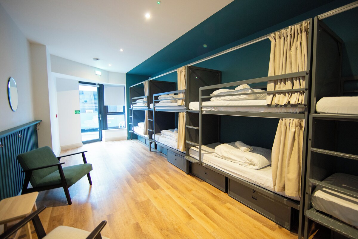 A dormitory room with bunk beds, a desk, and a chair.