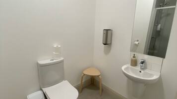 A small, modern bathroom with a toilet, sink, and a small stool.
