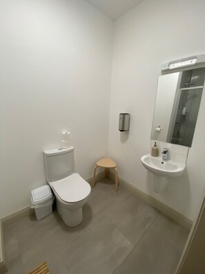 A small, modern bathroom with a toilet, sink, and a small stool. - Heyday Hostel (Ballina)