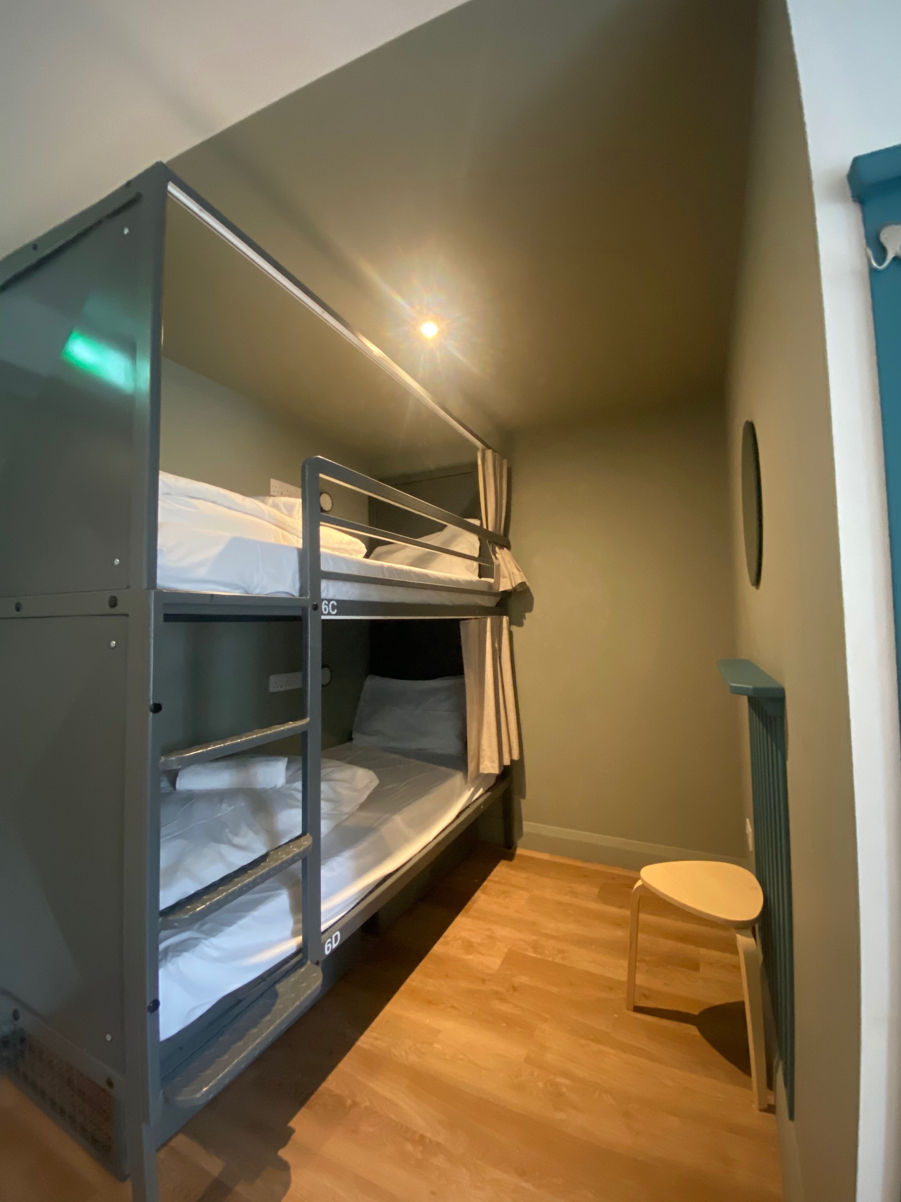 A bunk bed room with a small stool, a radiator, and a light fixture on the ceiling.