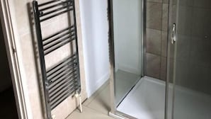 A bathroom with a glass shower enclosure, a towel rack, and a tiled floor.