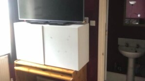 A room with a television on a wooden stand, a white cabinet, a door leading to a bathroom, and a radiator.