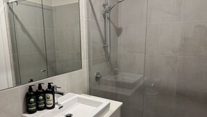A bathroom with a glass-enclosed shower, a white sink, and three bottles of StayMint body wash.