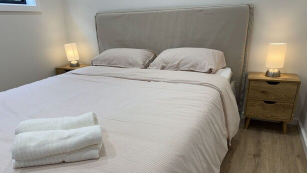 A neatly made bed with a folded towel, two bedside tables with lamps, and a wooden floor.