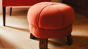 Un fauteuil rouge et un pouf dans une pièce dont le sol est recouvert de carreaux et qui contient des meubles en bois.