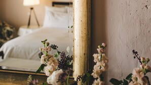 Un dormitorio con cama, mesita de noche, lámpara y espejo que refleja la habitación.