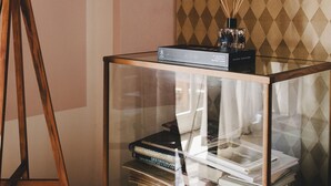 Una mesita auxiliar con tapa de vidrio, una pila de libros, una lámpara y un objeto decorativo encima.