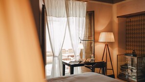 Habitación de hotel con una cama, un escritorio con lámpara, una estantería y vistas al exterior.