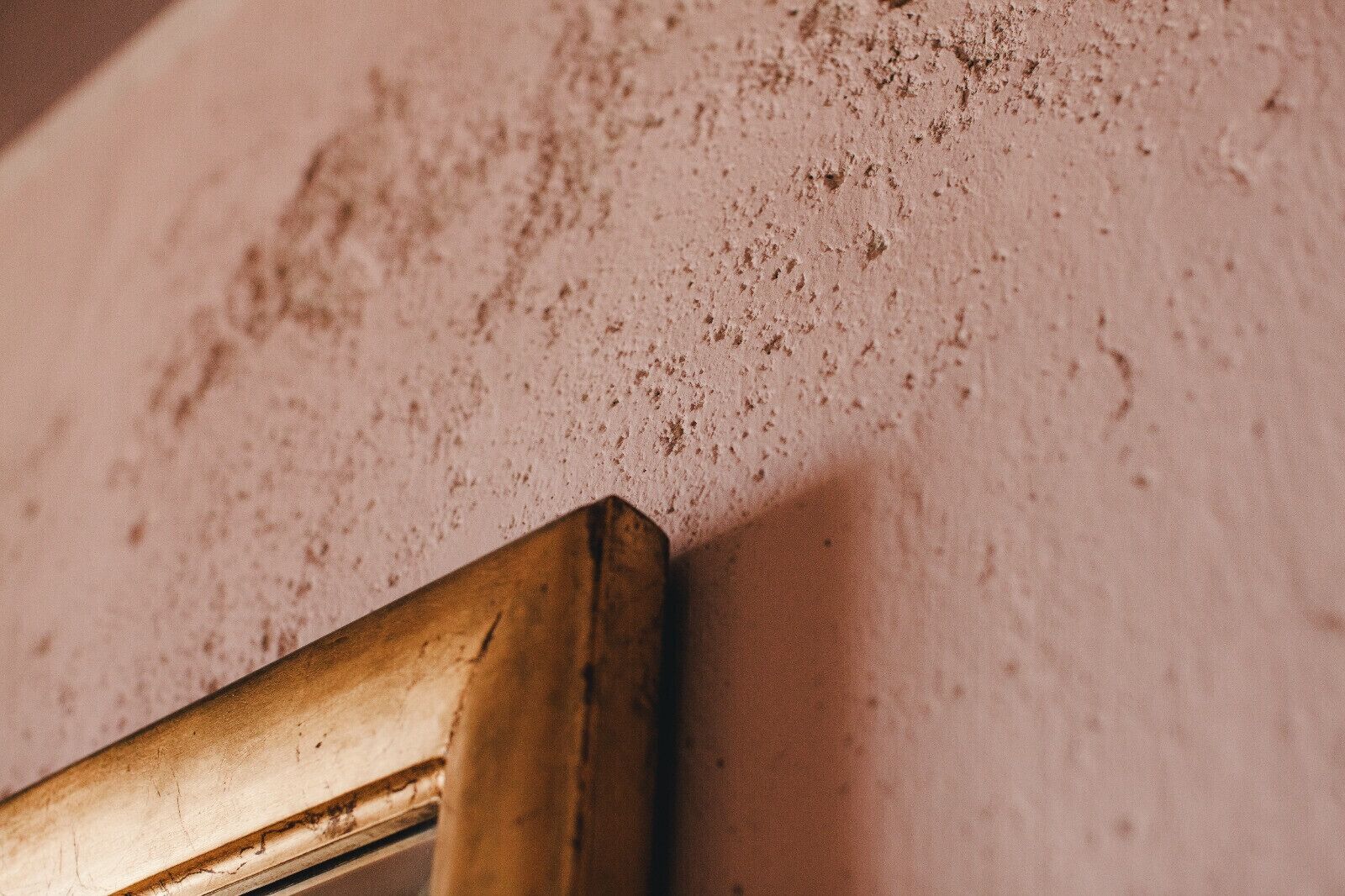 A close-up of a wall with a textured surface and a corner of a wooden object, possibly furniture.
