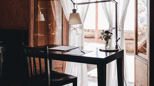 A wooden desk with a lamp, a chair, and a vase with flowers. - Red Room (Praiano)