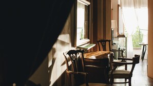 A room with a wooden table and chairs, a window with curtains, and a view of greenery outside. - La Grigia (Praiano)