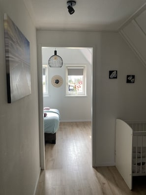 Un couloir menant à une chambre à coucher équipée d’un lit, d’une fenêtre et d’un berceau.